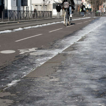 female silhouette riding a bicycle on city bike lanes in sunny winter time, icy pavement on the foreground, square imageの写真素材