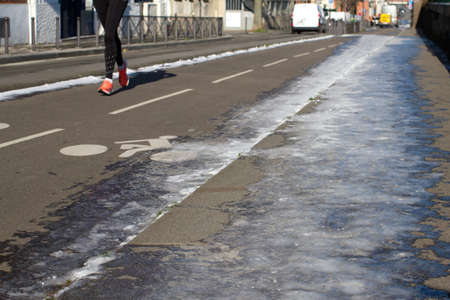 silhouette of anonymous female jogger running on partly frozen city bicycle lanes in sunny winter timeの写真素材