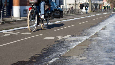 anonymous woman riding a bicycle on partly icy and snowy city bike lanes in sunny winter timeの写真素材