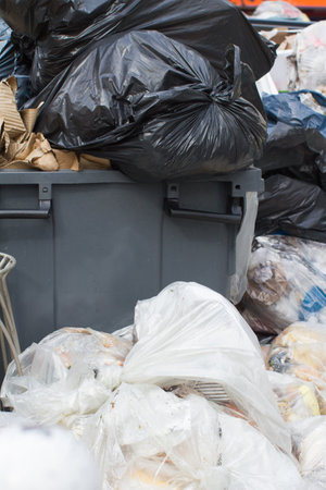 closeup of plastic garbage bags loaded with food and junk overflowing a Paris rubbish containerの写真素材