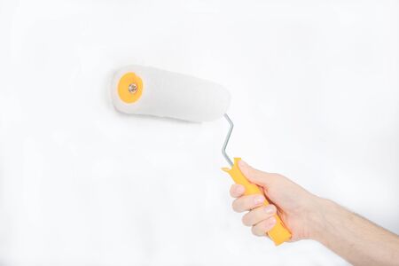 A young guy is painting a white wall. Holds the roller in his hand. Builder. Repairs.