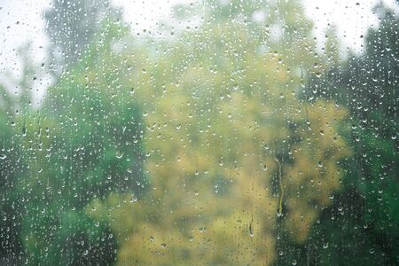 raindrops on glass, on a background of clouds. Green treesの写真素材