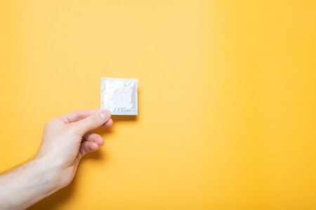 The girl holds a condom in hand. Yellow background, place for text.