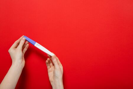 Female hands hold a pregnancy test on a red background. Place for text