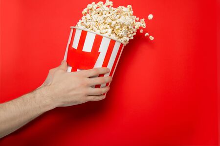 The guy holds popcorn in his hands on a red background. Place for text.の写真素材