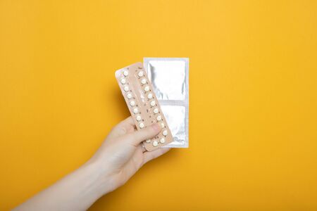 The girl holds contraceptive pills and condoms in her hands. Contraception. Yellow background place...