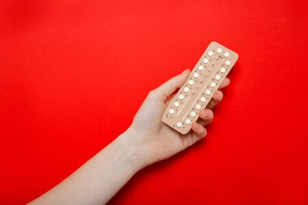 Girl holds birth control pills in her hands. Contraception. Red background, place for text.