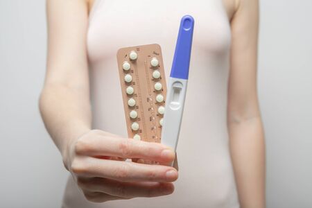 The girl holds a pregnancy test in her hands and birth control pills. Close-upの写真素材