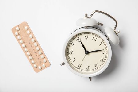 Female birth control pills and alarm clock on a white backgroundの写真素材