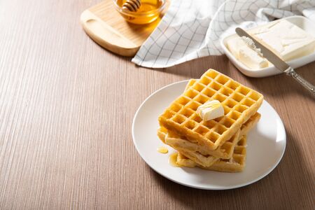 Plate with delicious waffles with honey and a slice of butterの写真素材