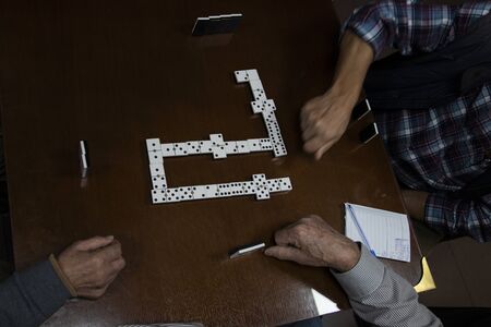 Men playing game of dominoes on wooden table with glass in senior centerの写真素材