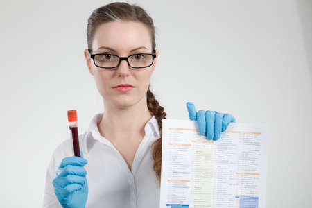 young woman with medical gloves and medical face mask holding a blood sample and an analyzing form