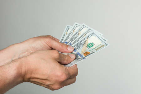 man's hand with a bunch of hundred dollar bills in front of a gray backgroundの写真素材