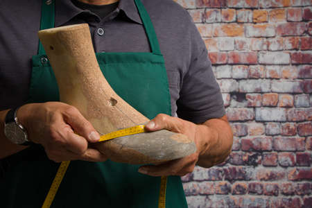 close up of hands of orthopedic shoemaker controlling an individual wooden last with a measurement tapeの写真素材