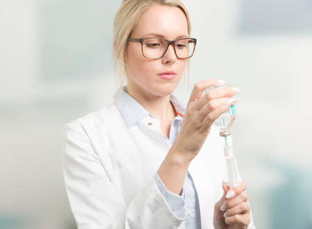 young female doctor or doctor's assistant or student pulls up a syringe with clinic room in backgroundの写真素材