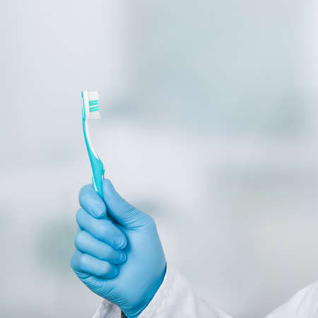 Dentist's hand in blue gloves prenting a tooth brushの写真素材