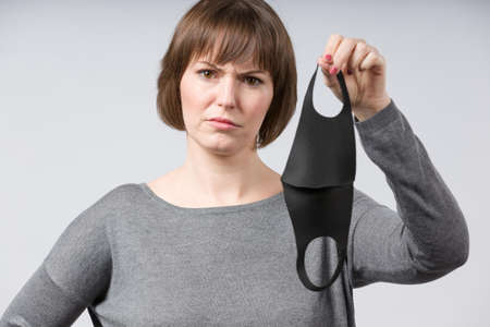 young woman shows a simple non medical face mask making a wry faceの写真素材