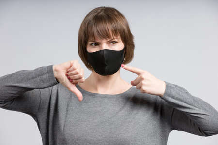 young woman shows a simple non medical face mask shows thumbs downの写真素材