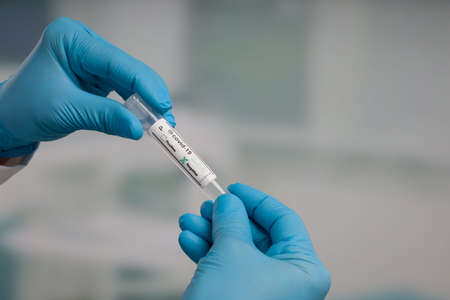 close-up of hand in blue gloves holding an empty test tube for virus analysis with result markers in...