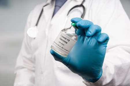 Close-up of doctor's hand in medical gloves with a bottle of Covid-19 serum / vaccine for...