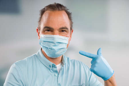 Doctor with medical face mask and medical gloves is pointing to his face mask