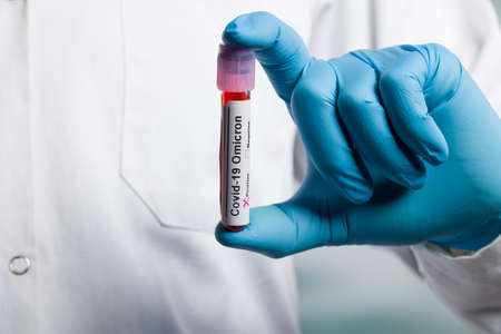 Close up of hands in medical gloves holding a test tube after virus analysis with omicron result...