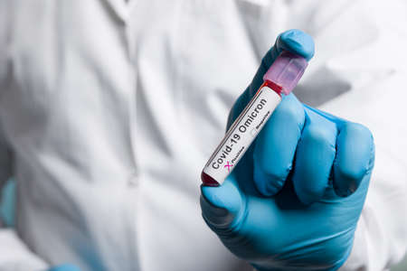 Close up of hands in medical gloves holding a test tube after virus analysis with omicron result...