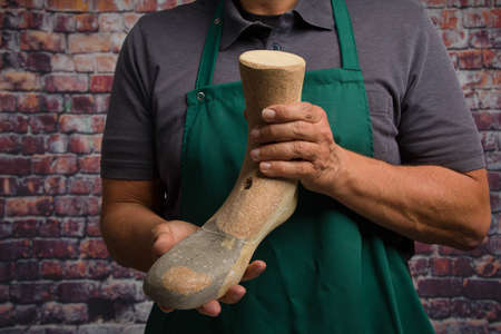 close up of hands of orthopedic shoemaker presenting an individual wooden last in his workshop