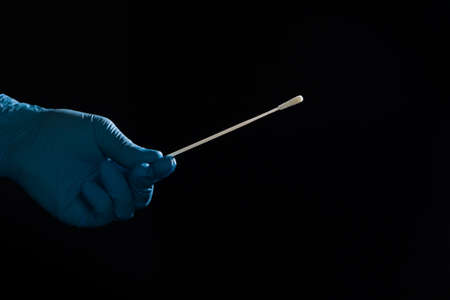 Close up of doctor's hand handling a smear test or swab test in front of a black background