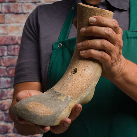 close up of hands of orthopedic shoemaker presenting an individual wooden load in his workshop wall