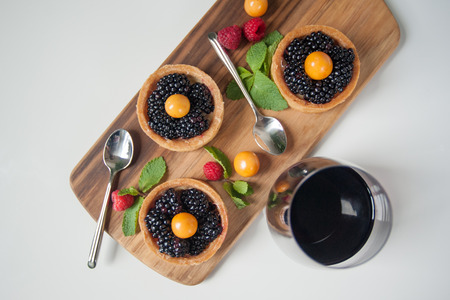 Delicious fruit tarts made with blackberries and gooseberries displayed on a wooden board and garnished with mint, raspberries. Paired with a glass of red wine.の写真素材