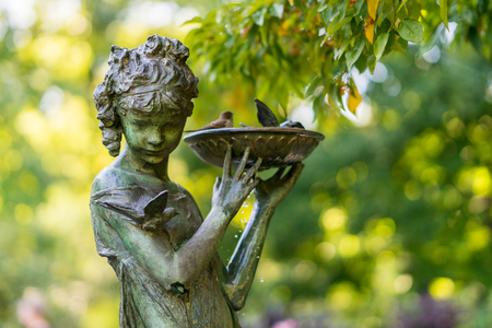 Sculpture of a girl with a bird bath, fountain. Natural setting with a bronze fountain statue in a garden, New Yorkの写真素材