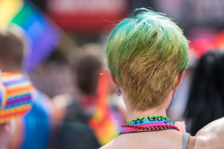 Young woman with green hair in a crowd celebrating Pride Parade. Wearing bright rainbow ribbons. Supporting marriage equality and LGBT rights.の写真素材