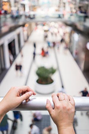 Point of view of a female standing on a second floor of a shopping mall looking down. Two hands visible in the frame.の写真素材