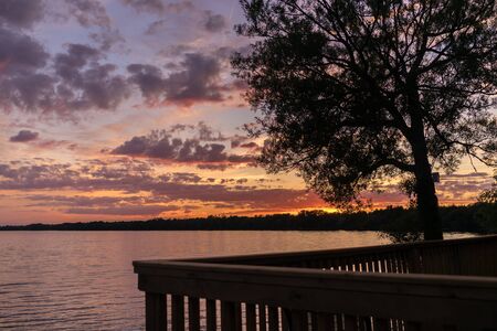Beautiful summer sunset with a colorful sky and clouds, reflection on the surface of the lake. Relaxing cottage weekend.の写真素材