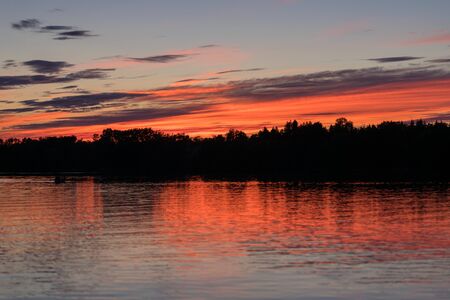 Beautiful summer sunset with a colorful sky and clouds, reflection on the surface of the lake. Relaxing cottage weekend.の写真素材