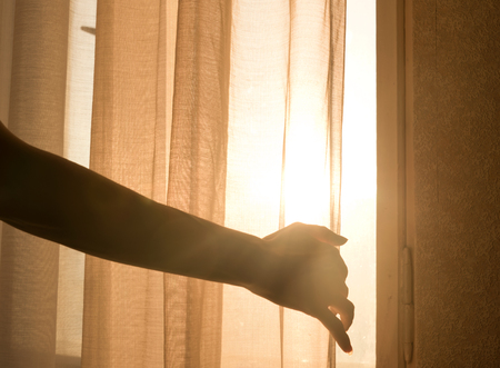 Female arm reaching out to open a curtain - warm sun light shining throughの写真素材