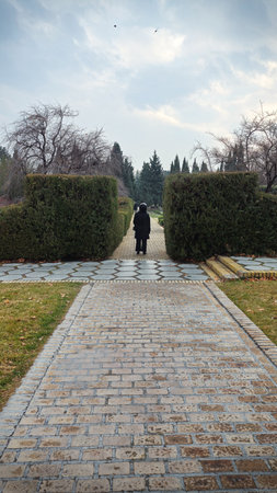 A young woman in a black coat walks along a stone path in the park.の写真素材