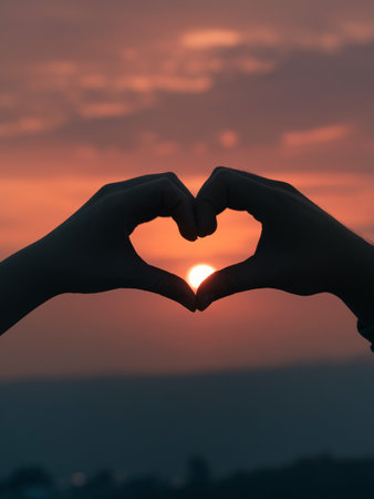 Silhouette of hands forming a heart shape on sunset sky backgroundの素材