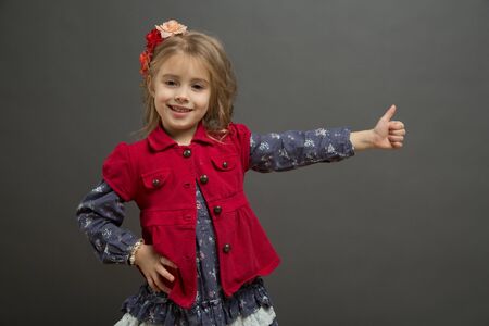Sweet little girl in a red and blue dress gives thumbs upの写真素材