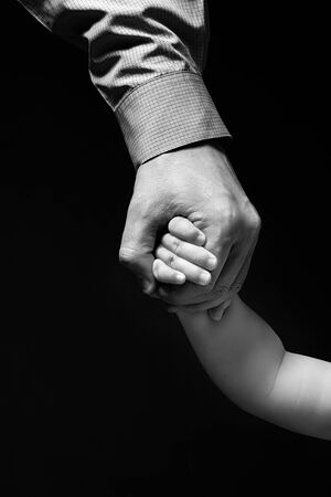 Father's hand holding child's hand. Hand businessman in shirt holding a child's hand. Isolated on black background. Grayscale.の写真素材