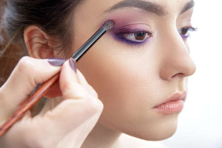 Stylist hand applying eyes make-up to the eyelids of a young beautiful model.
