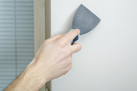 Male hand holds putty knife on the wall near the corner. Finishing work.の写真素材