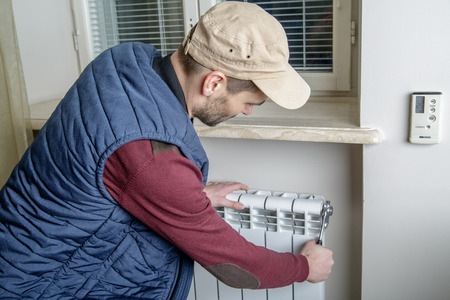 Male plumber repairing radiator with wrench. Worker looking at the radiator. Close-up.の写真素材