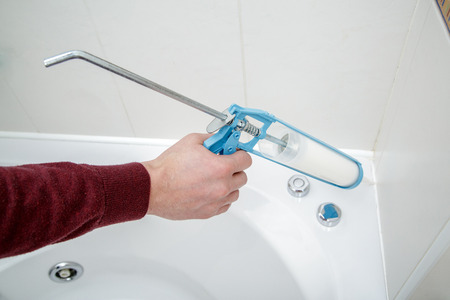 Plumber hand applying silicone sealant with caulking gun in the bathroom.の写真素材