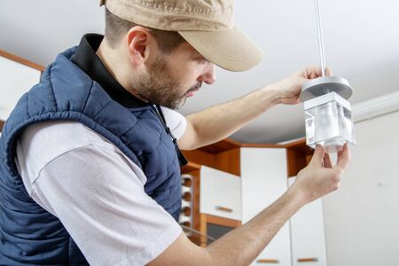 A male electrician fixing light on the ceiling. Worker changing a light bulb in the kitchen. Close-up.の写真素材