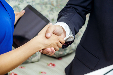 Businessman and business lady shake hands. The male in a suit and a white shirt. The woman in a blue blouse. A tablet in her second hand.の写真素材