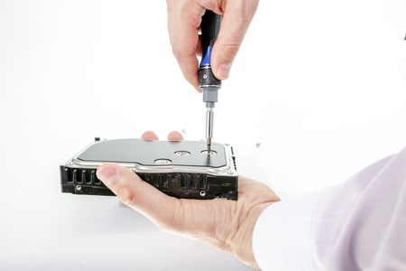 Man's hand holds 3.5 HDD. His another hand unscrews the hard drive case with a screwdriver. Isolated on white background.の写真素材