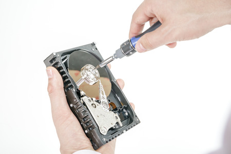 Man's hand holds open 3.5 HDD. His another hand unscrews the cover of the engine with a screwdriver. Isolated on white background.の写真素材