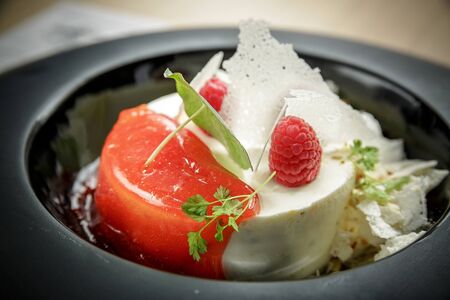 Ice cream dessert with raspberries, jelly and greenery on a black plate.の写真素材